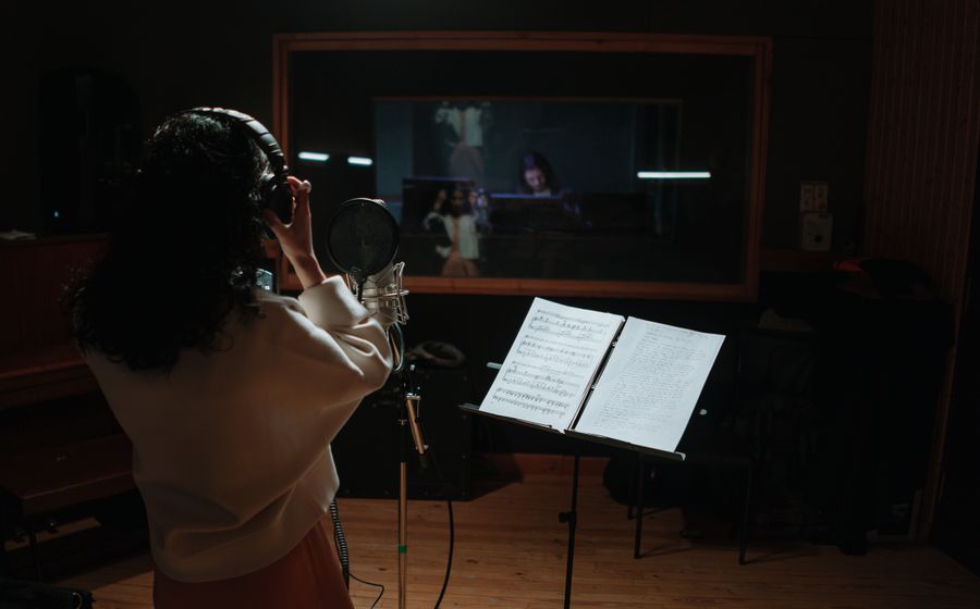 A singer recording vocals at a microphone in a music studio